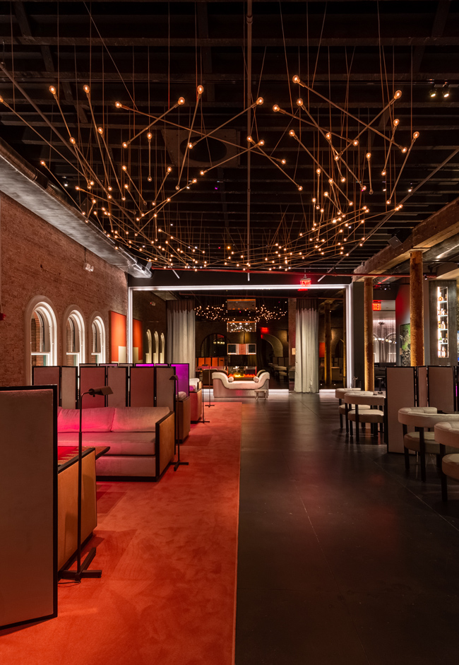 A bespoke chandelier lights the velvet red carpet of a lounge space